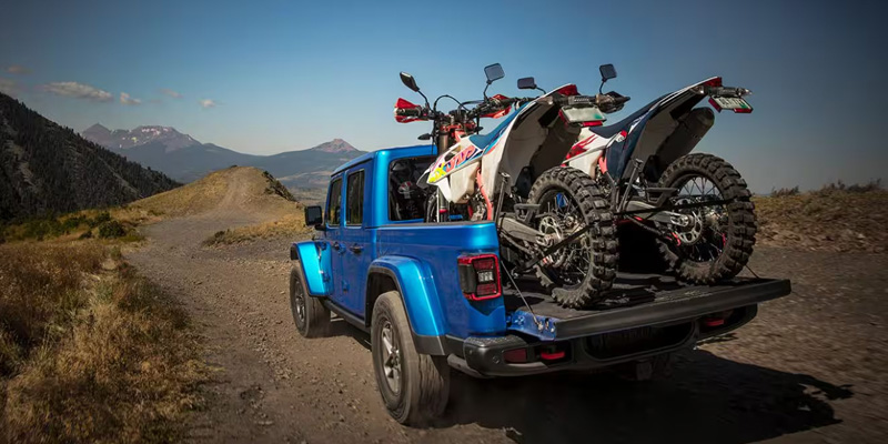 A photo of a blue 2025 Jeep Gladiator with dirt bikes in the bed.