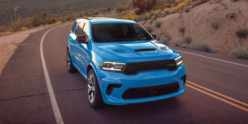 Blue Dodge Durango SUV driving on a winding road through a desert landscape.
