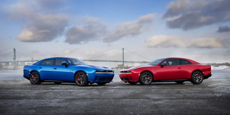 Blue and red Dodge Charger vehicles parked side by side near a waterfront bridge.