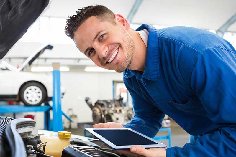 Technician inspecting a vehicle engine with a digital tablet during automotive service.