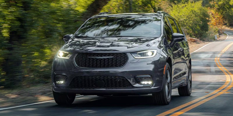 Black Chrysler Pacifica minivan driving on a scenic road surrounded by trees.