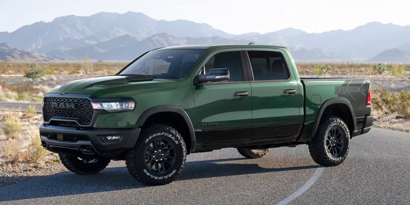 Green RAM 1500 pickup truck parked on a road with mountains in the background.