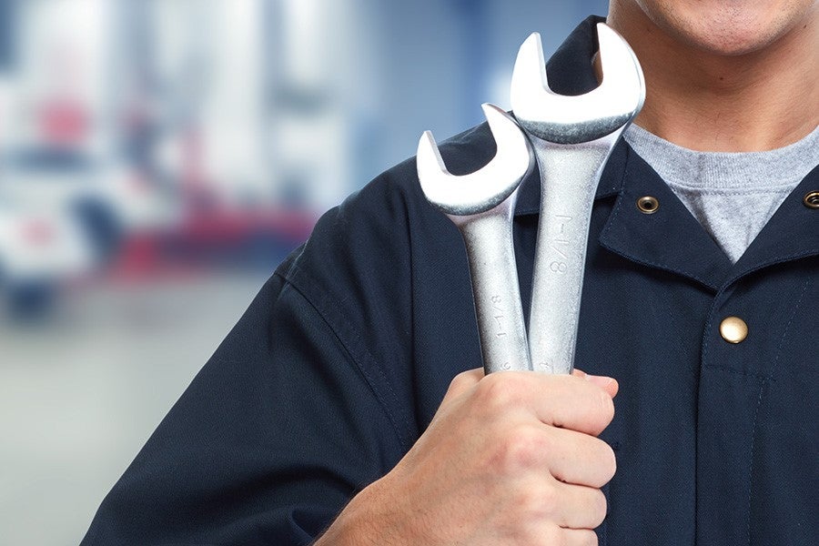 Automotive technician holding wrenches during vehicle repair service.